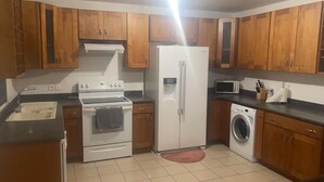A kitchen with wooden cabinets, a refrigerator, a stove, a microwave, and a washing machine. - Spacious apartment with pool and gorgeous views of Marigot! (Marigot)