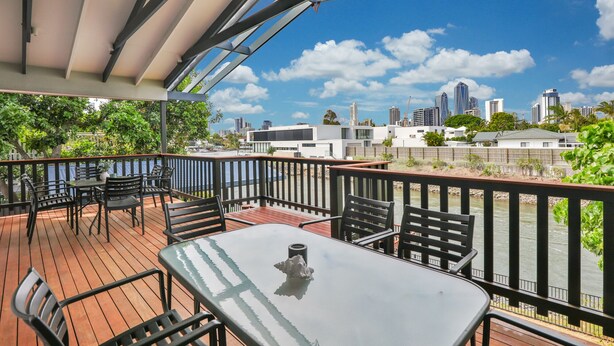 A covered outdoor area with a table and chairs, overlooking a cityscape with modern buildings.