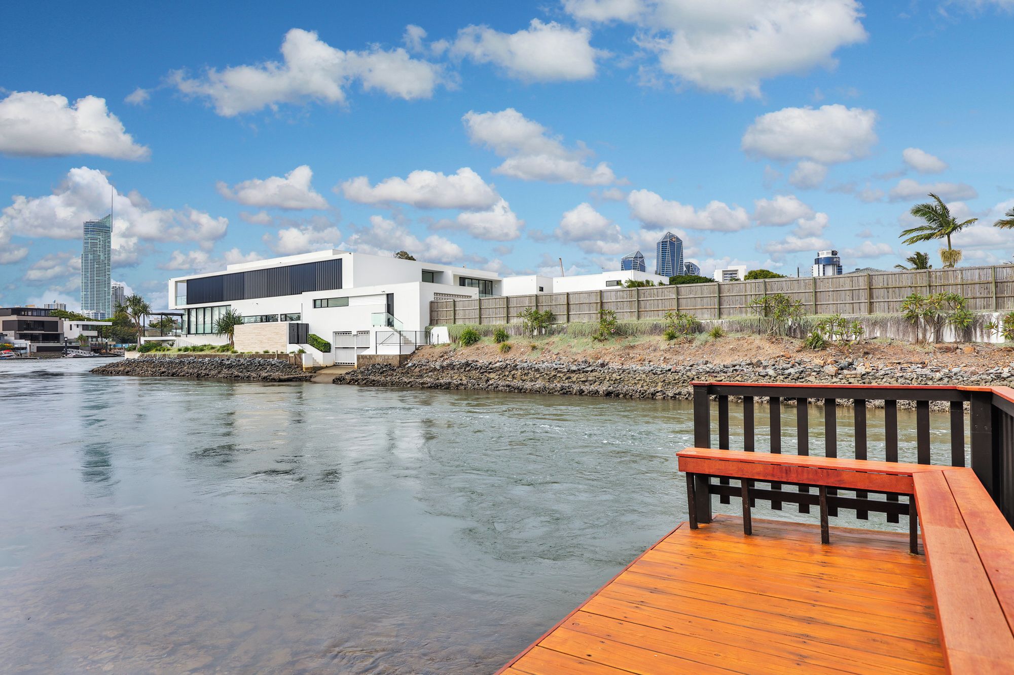 A waterfront property with a modern white building, a wooden deck, and a view of the city skyline.
