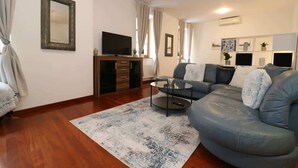 Een woonkamer met een bank, een bijzettafeltje, een televisie op een houten kast en een kamerkleed met dessin.