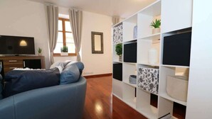 Een moderne woonkamer met een blauwe bank, een flatscreentelevisie en een witte boekenkast met decoratieve objecten.