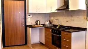A compact kitchen with wooden cabinets, a stove, and a sink. - Renos Butik Otel (Mersin)