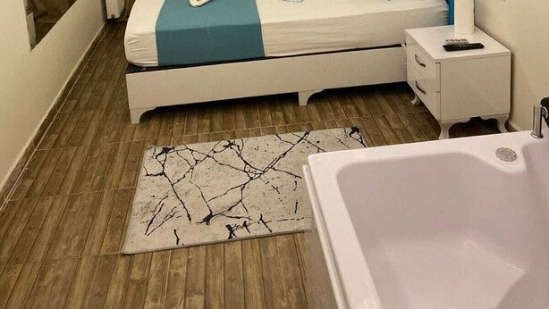 A modern bedroom with a skylight, a bed with blue and white bedding, a bedside table with a remote control, and a bathroom with a bathtub. - Renos Butik Otel (Mersin)