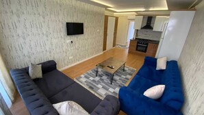 A modern living room with a sofa, a blue couch, and a flat-screen TV mounted on the wall. - Renos Butik Otel (Mersin)