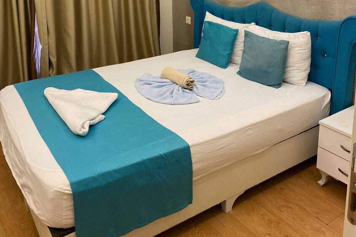 A neatly made bed with a blue headboard, white pillows, and a teal bedspread.