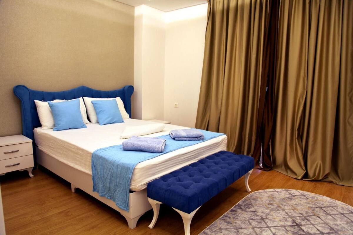 A neatly arranged bedroom with a bed, bedside tables, a bench, and a patterned rug.