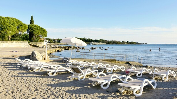 A beach with white lounge chairs and umbrellas, a rocky shoreline, and a clear blue sky. - New apartment, Anja, near the sea, Zambratija (Zambratija)