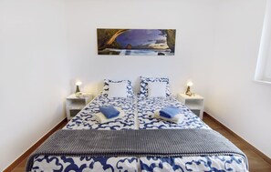 A double bed with a patterned bedspread, two bedside tables with lamps, and a painting above the bed.