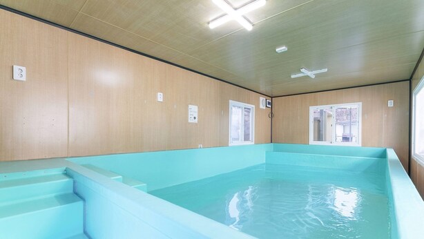 Una piscina con escalones de acceso, paredes de madera y luces en el techo.