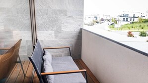Een balkon met een houten vloer, een ronde tafel met een roze object en een grijze bank.
