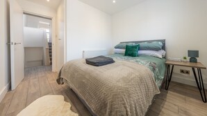 A bedroom with a bed, bedside table, and a view of a staircase. - Stylish split-level 2BR near Queen’s Park – bright, modern & well-connected (London)