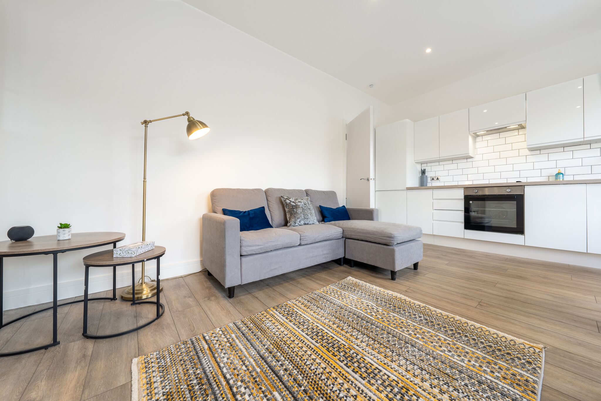 A modern living room with a grey sectional sofa, a small round table, a floor lamp, and a patterned rug.