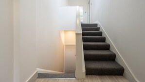 A staircase with carpeted steps and a white handrail, leading to a door at the top. - Stylish split-level 2BR near Queen’s Park – bright, modern & well-connected (London)