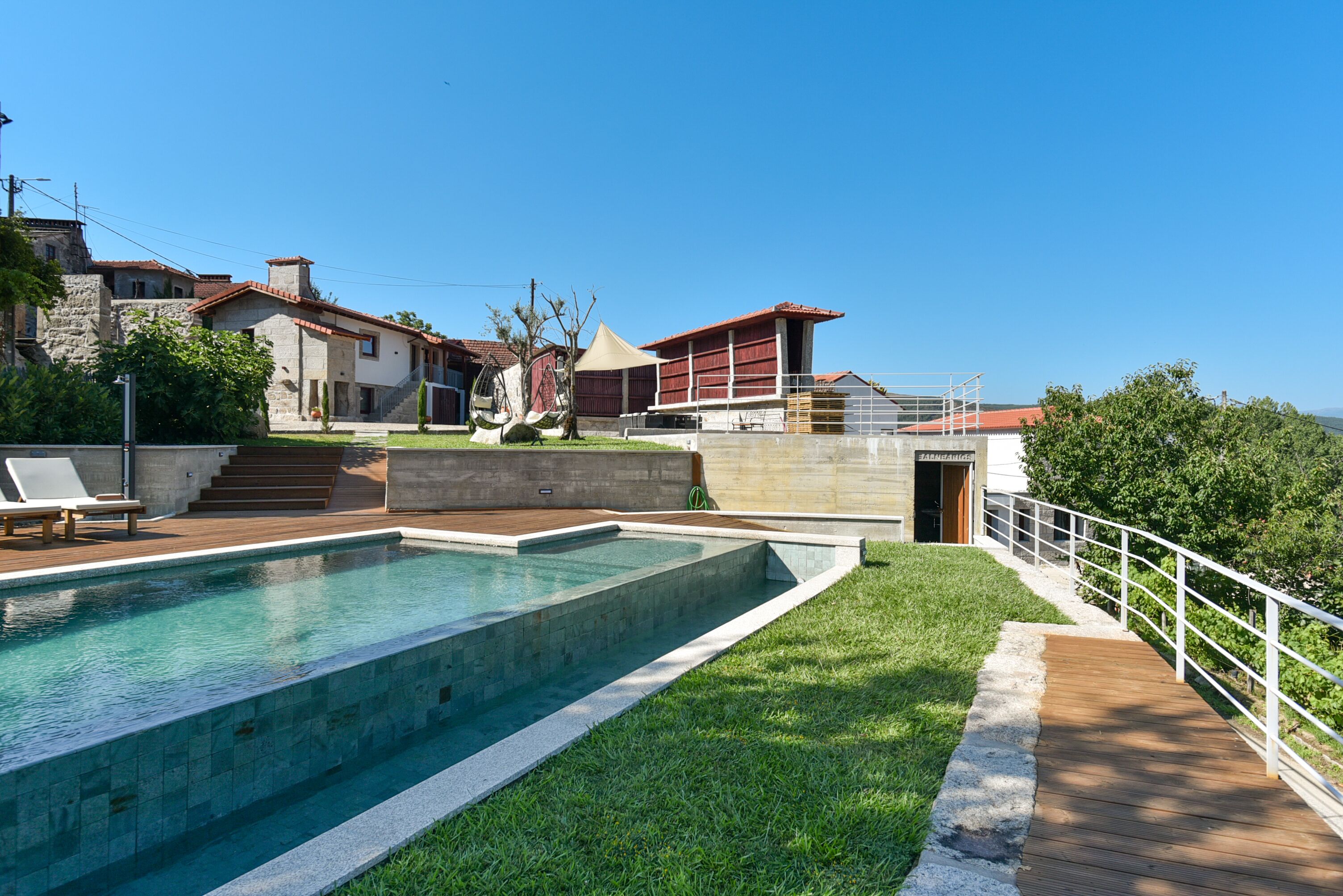 A swimming pool with a wooden deck, a stone building, and a red-roofed structure.