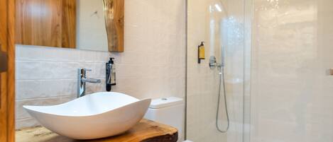 Een badkamer met een houten wastafelmeubel, een witte wasbak, een toilet en een douche met glazen wanden.