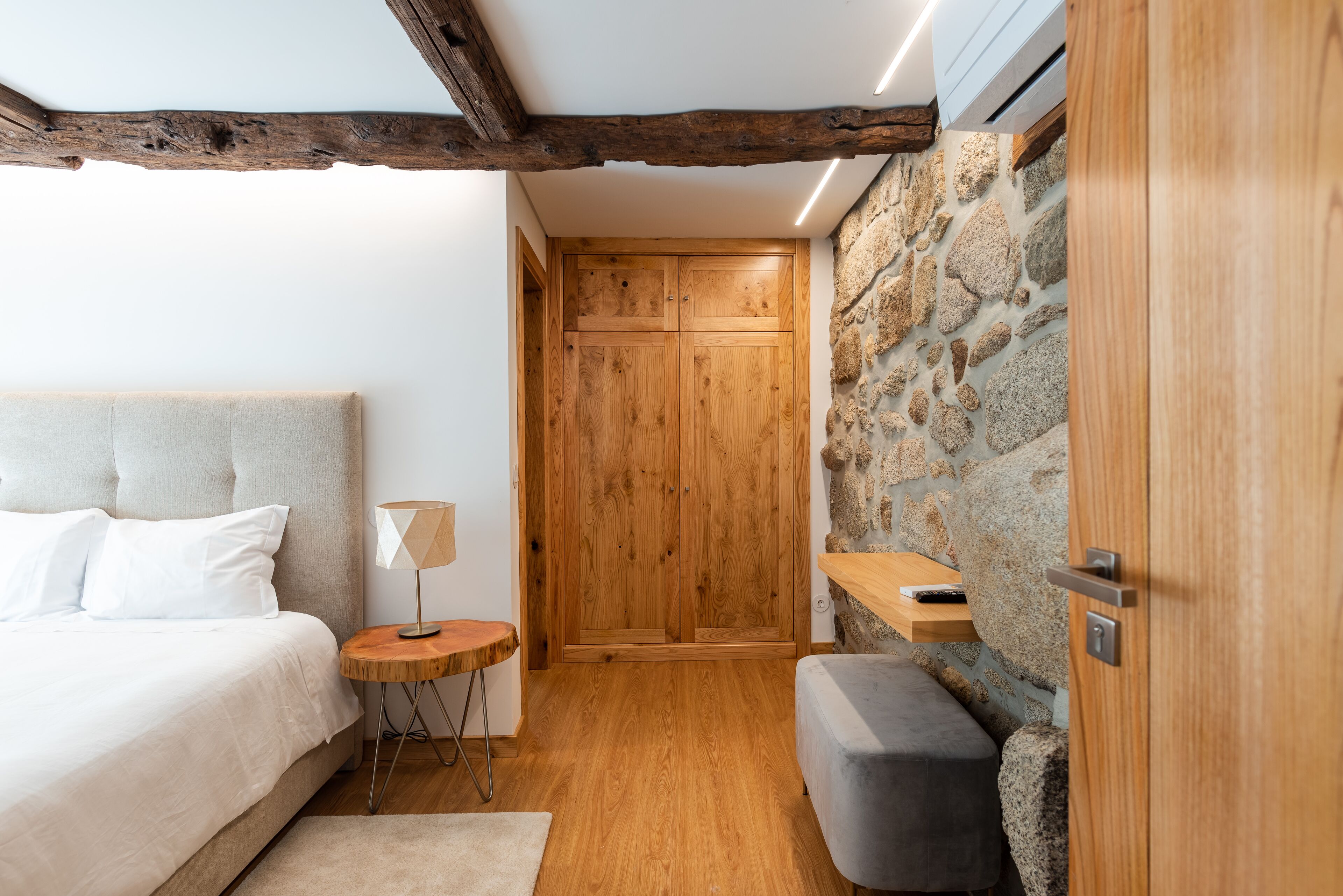 A bedroom with a bed, a bedside table, a lamp, a bench, and a wardrobe.
