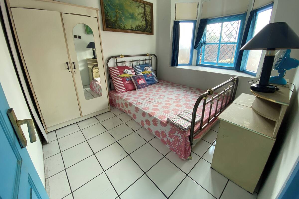 Un dormitorio pequeño y ordenado con una cama individual, un armario, un escritorio y una ventana con cortinas.