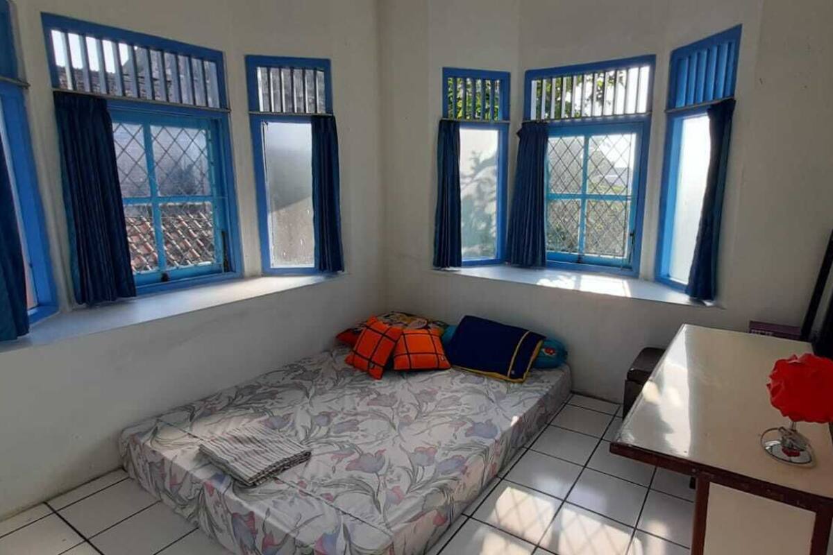 Una habitación pequeña y sencilla con cama, mesa y ventana con cortinas.