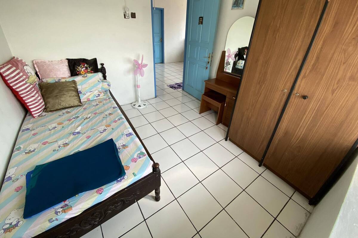 Un dormitorio con una cama, un tocador, una puerta azul y un ventilador.