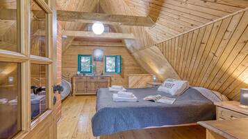 Um quarto de sótão acolhedor, com teto inclinado, paredes de madeira, uma cama com colcha azul, uma mesa de cabeceira e uma janela com vista.