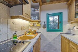Une cuisine de taille réduite, dotée de meubles en bois, d’un évier et d’une fenêtre au cadre de couleur turquoise.