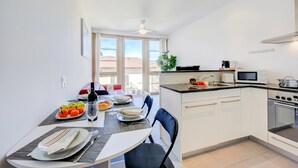 A modern kitchen with white cabinets, a dining table set with plates, glasses, and a bottle, and a view of buildings outside. - Residenza Castello Flat With A/C and Garage (Mendrisio)
