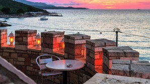 A seaside terrace with stone walls, a table, and chairs, overlooking the sea and a sunset. - Hotel Castle (Ksamil)