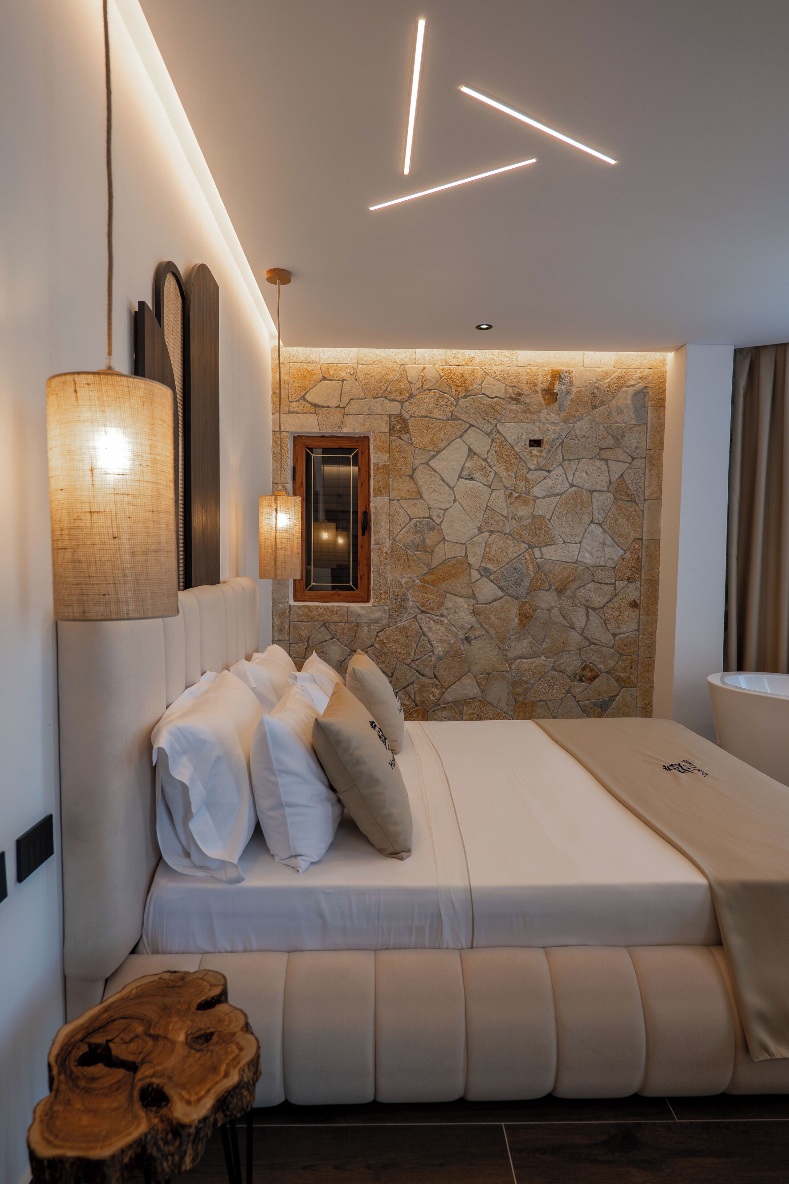 Ein modernes Schlafzimmer mit Steinsandsteinwand, einem Bett mit weißen Leinen, einem Holznachttisch und einer Pendelleuchte.