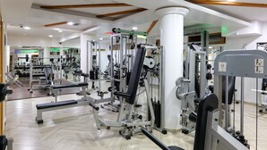 A gym with various exercise machines, a mirrored wall, and wooden ceiling beams. - Hotel Castle (Ksamil)