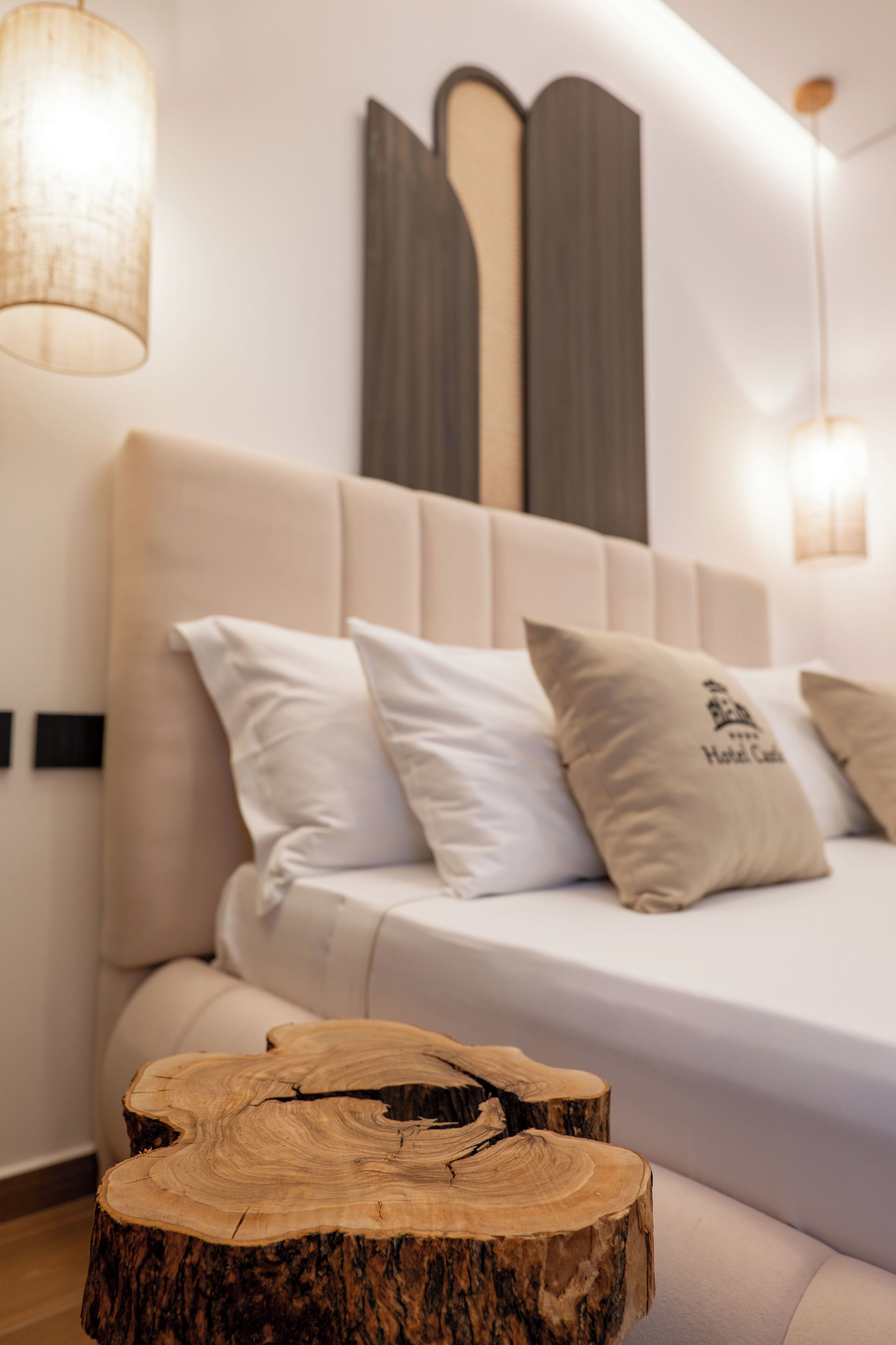 A modern bedroom with a large bed, two bedside lamps, and a wooden tree stump table.