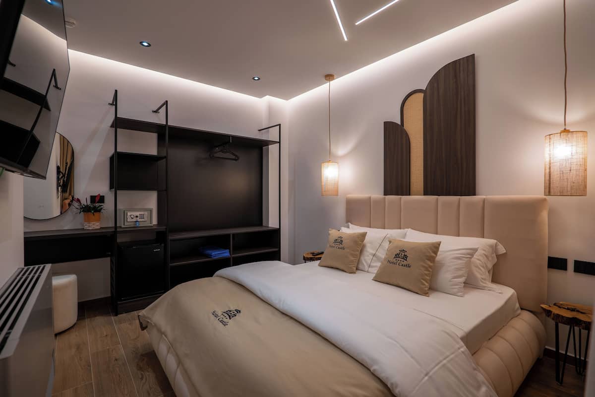 A modern hotel room with a large bed, a desk with a computer, a TV, and a wardrobe.