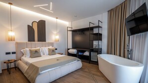 A modern hotel room with a large bed, a freestanding bathtub, a TV mounted on the wall, and a walk-in closet. - Hotel Castle (Ksamil)