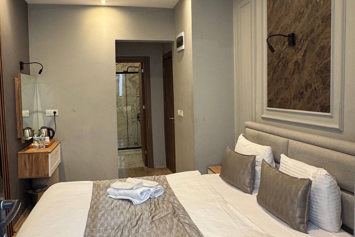 A hotel room with a large bed, a bedside table with a lamp, a mirror, and a marble wall.