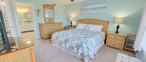 A bedroom with a bed, two nightstands, a ceiling fan, a dresser, a mirror, and a painting on the wall.