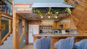 Une cuisine avec des meubles de rangement en bois, un réfrigérateur, un four à micro-ondes et des tabourets de bar.