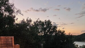 Une terrasse dotée d’un foyer, d’un espace salon et offrant une vue sur un plan d’eau et des arbres.