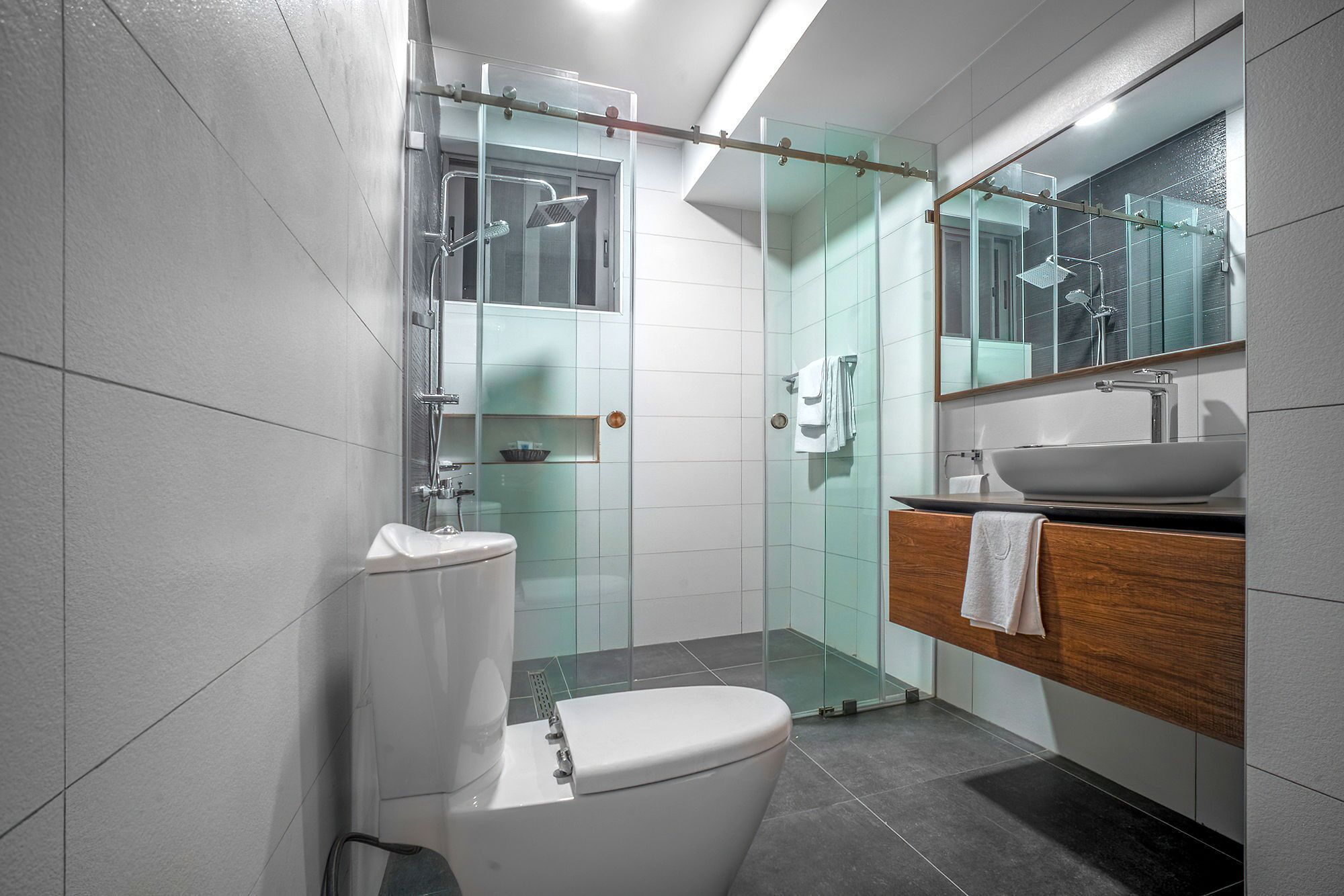 A modern bathroom with a glass-enclosed shower, a white toilet, and a wooden vanity with a sink.