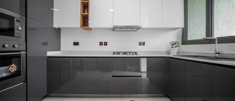 A modern kitchen with dark cabinets, a built-in oven, a microwave, and a stainless steel range hood.