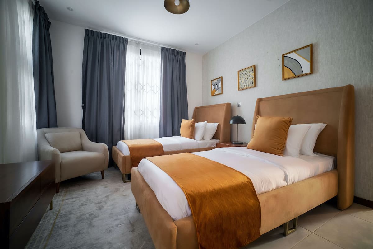 A hotel room with two beds, a sofa, a desk, and a large window with curtains.
