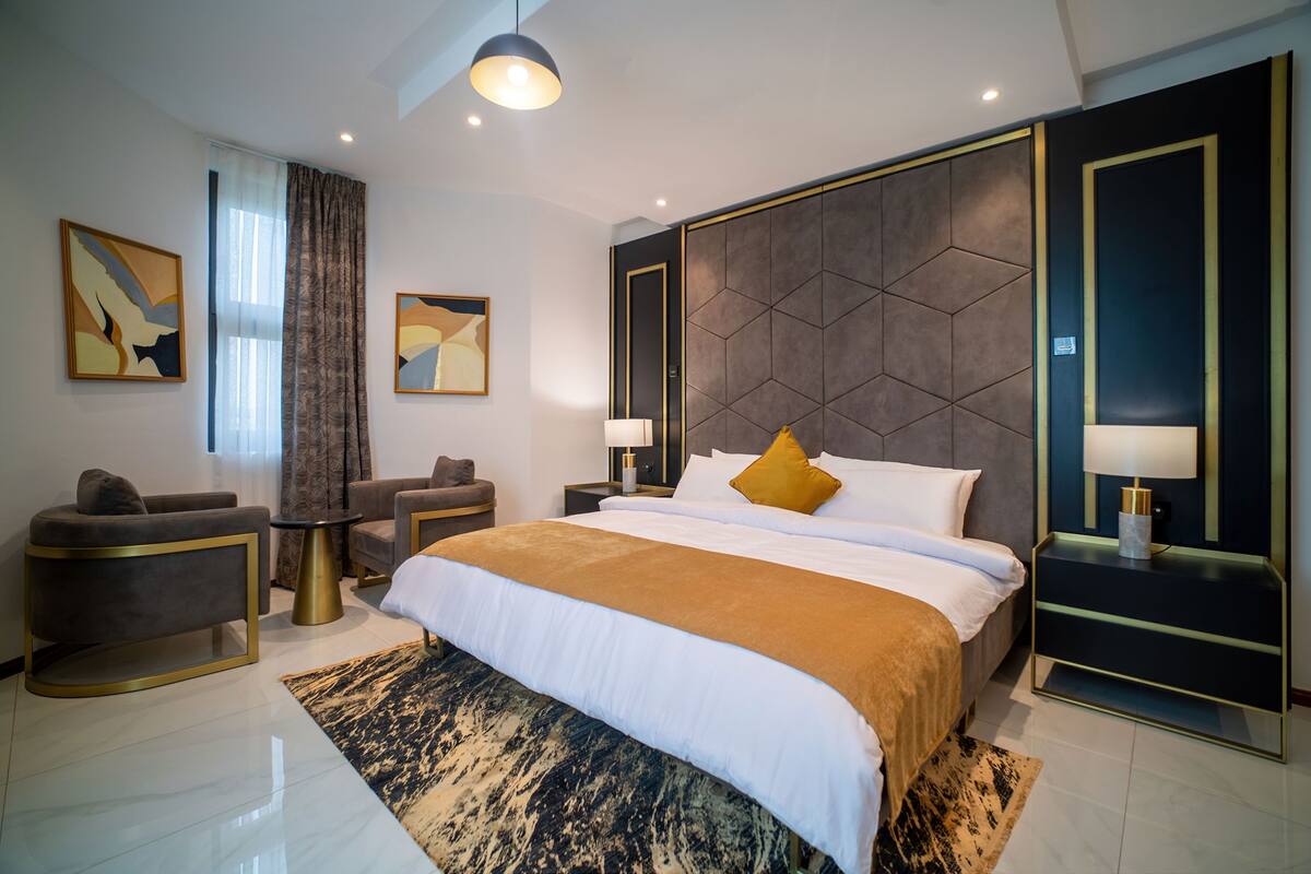A modern hotel room with a large bed, a sofa, a desk, and a chair.