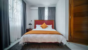 A neatly made bed with a red headboard, a grey curtain, and a wooden door.