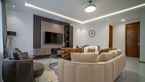 A modern living room with a curved sofa, a small round table, and a flat-screen TV mounted on the wall. - Alexander Palace Hotel Apartment (Amrahia)
