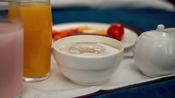 A tray with a glass of orange juice, a bowl of cereal, a small plate with a cherry tomato, and a teapot.