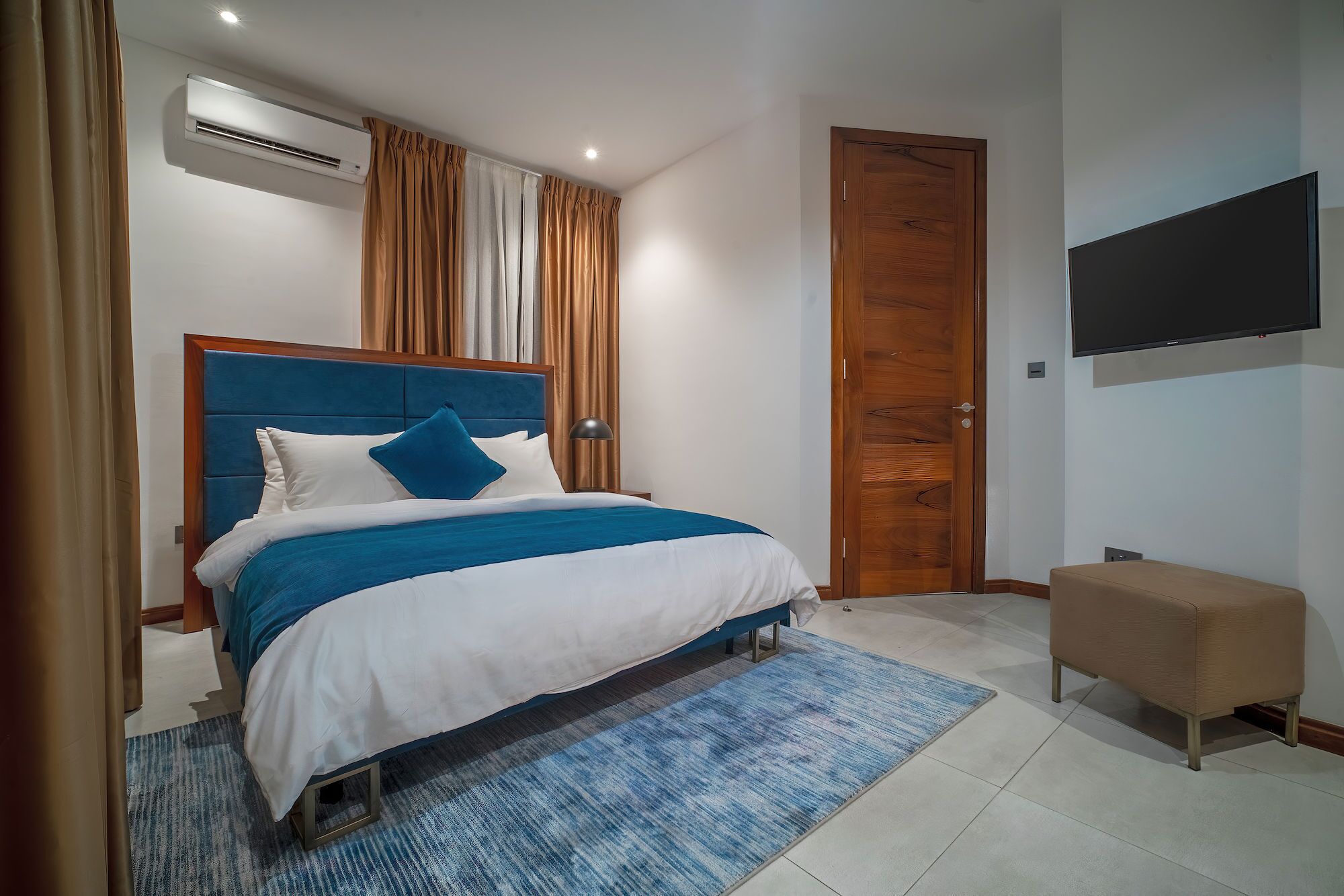 Un dormitorio con una cama, televisor, puerta de madera y aire acondicionado.