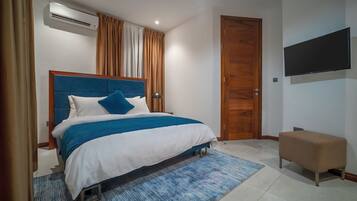 A bedroom with a bed, a TV, a wooden door, and an air conditioning unit.