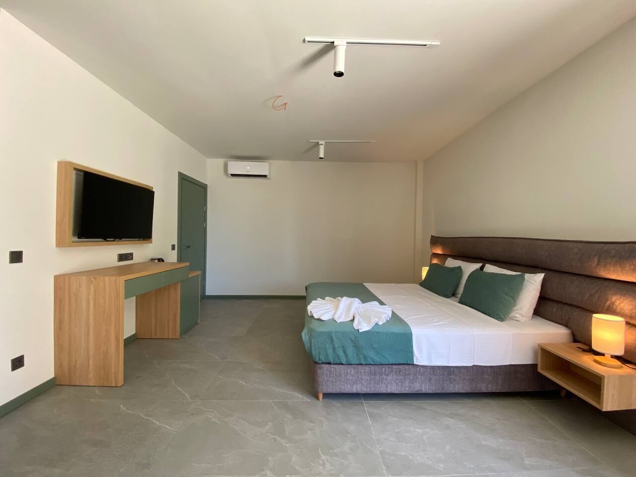 A modern hotel room with a bed, a desk, a television, and a door.