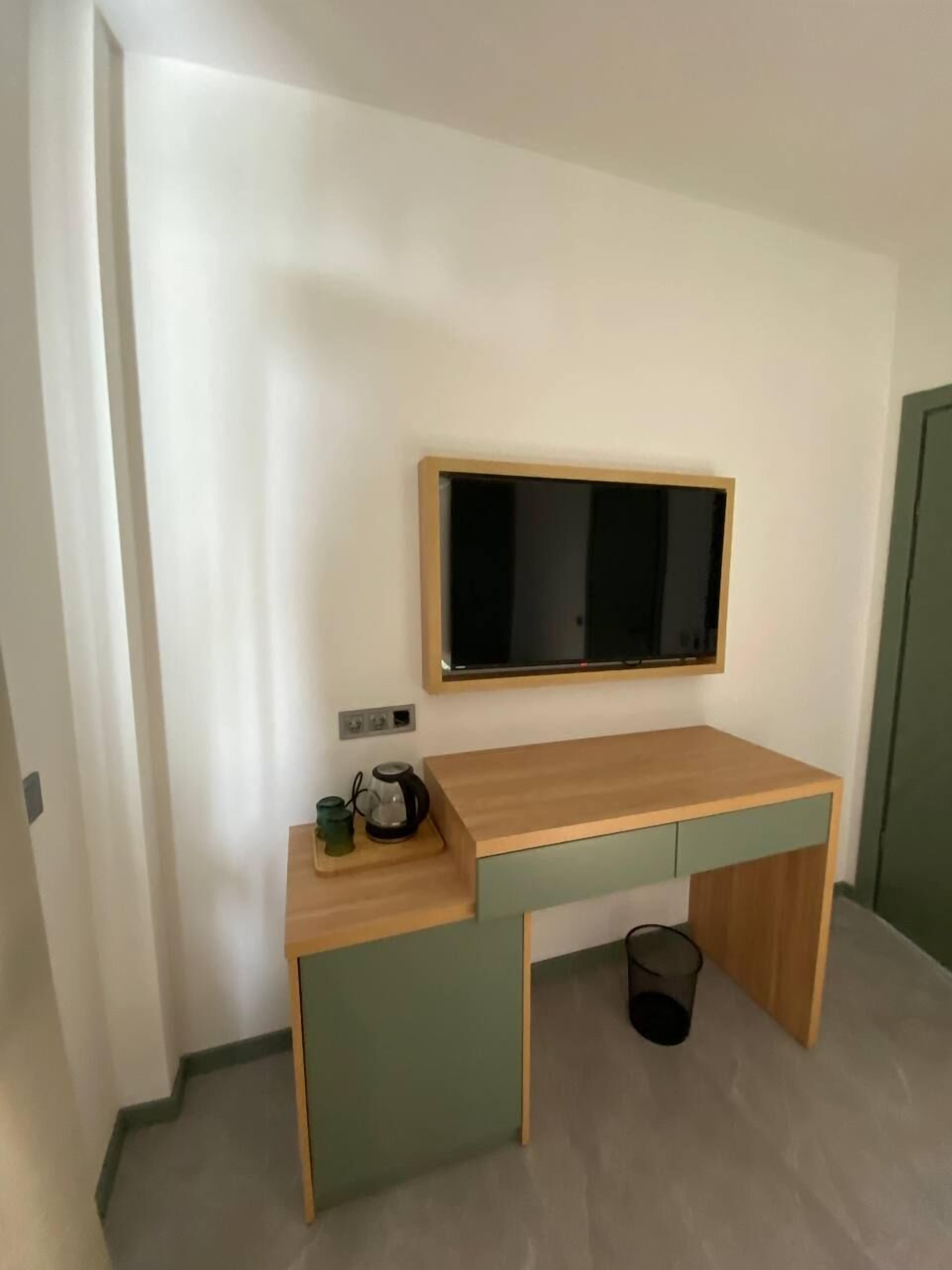 Una habitación pequeña y moderna con un escritorio de madera, un televisor montado y un cesto de basura.