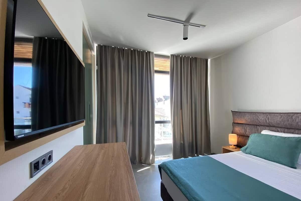 Una habitación de hotel con cama, escritorio, televisor y cortinas.