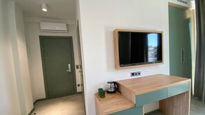 A modern hotel room with a wooden desk, a flat-screen TV mounted on the wall, and a green door. - H2O Ureki (Ureki)