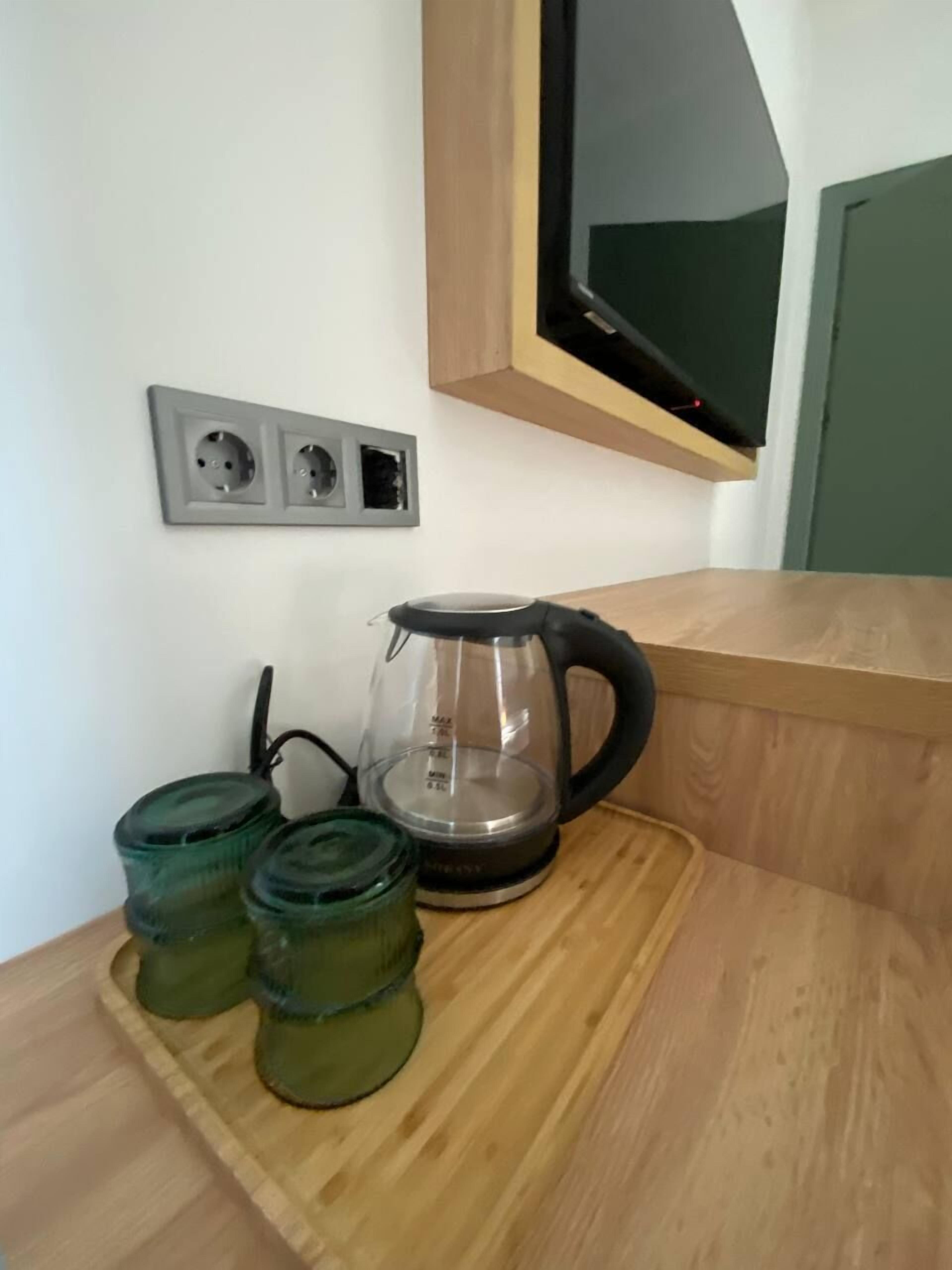 Uma área de cozinha com bancada de madeira, uma cafeteira de vidro e três potes de vidro verdes.